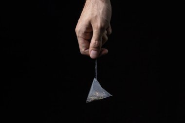 Siyah arka planda çay poşeti piramidi. Hızlı demleme çayı. Çay poşeti tutan bir adamın eli.