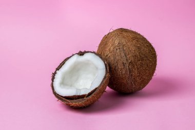 Pembe arka planda izole edilmiş hindistan cevizi. Görüntünün ortasında bir hindistan cevizinin yanında yarım hindistan cevizi. Sağlıklı meyve