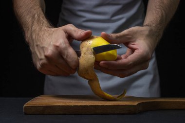 Siyah arka planda patatesler. Aşçı patatesleri bıçakla soyar. Erkek elleri patates soyarken