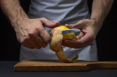Siyah arka planda patatesler. Aşçı patatesleri bıçakla soyar. Erkek elleri patates soyarken