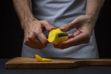 Siyah arka planda patatesler. Aşçı patatesleri bıçakla keser. Erkek eli siyah arka planda patates kesiyor.