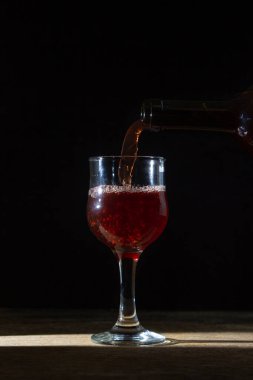 Ev yapımı kırmızı şarap koyu bir arka planda bir bardağa dökülür. Siyah arka planda bir kadeh kırmızı şarap. Alkolik içecek.