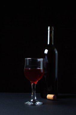 Koyu arkaplanda bir şişenin yanında bir bardak ev yapımı şarap. Siyah arka planda bir kadeh kırmızı şarap. Alkolik içki.