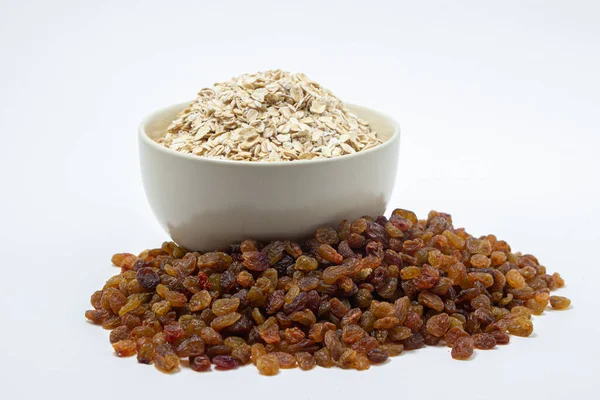 Beyaz arka planda yulaf ezmesi ve kuru üzüm. Sağlıklı beslenme. Bir fincan dolusu yulaf ezmesi, yakınlarda kuru üzümler. Düzgün beslenme kavramı