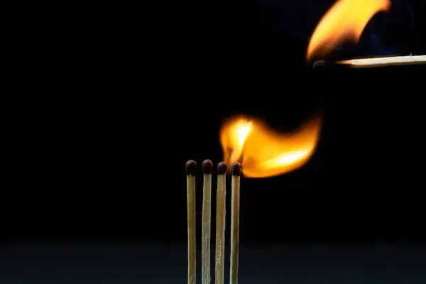 Burning match on a black background. A match sets fire to another match against a dark background. Burning in the dark