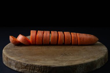 Koyu arkaplanda havuçlar. Siyah arka planda tahta bir tahtada dilimlenmiş havuçlar. Sağlıklı yemek.