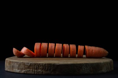 Koyu arkaplanda havuçlar. Siyah arka planda tahta bir tahtada dilimlenmiş havuçlar. Sağlıklı yemek.