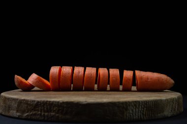 Koyu arkaplanda havuçlar. Siyah arka planda tahta bir tahtada dilimlenmiş havuçlar. Sağlıklı yemek.