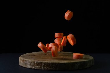 Koyu arkaplanda havuçlar. Dilimlenmiş havuçlar siyah arka planda tahta bir tahtaya düşer. Sağlıklı yemek.