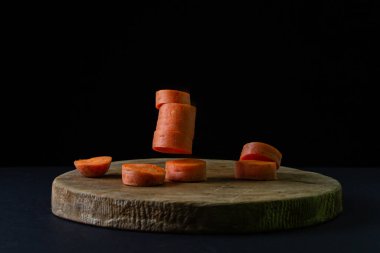 Koyu arkaplanda havuçlar. Dilimlenmiş havuçlar siyah arka planda tahta bir tahtaya düşer. Sağlıklı yemek.