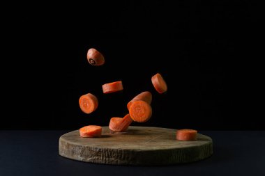 Koyu arkaplanda havuçlar. Dilimlenmiş havuçlar siyah arka planda tahta bir tahtaya düşer. Sağlıklı yemek.