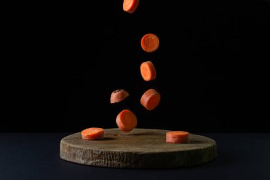 Koyu arkaplanda havuçlar. Dilimlenmiş havuçlar siyah arka planda tahta bir tahtaya düşer. Sağlıklı yemek.