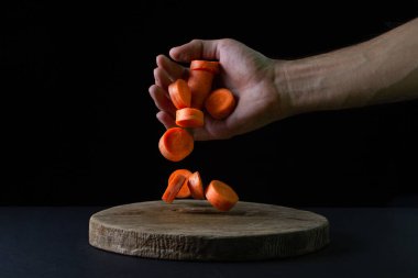 Koyu arkaplanda havuçlar. Kesilmiş havuçlar siyah arka planda bir adamın elinden düşüyor. Sağlıklı yemek.