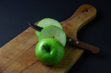 Siyah arka planda yeşil elma. Siyah arka planda kesme tahtasında kesilmiş yeşil bir elma. Sağlıklı yemek.