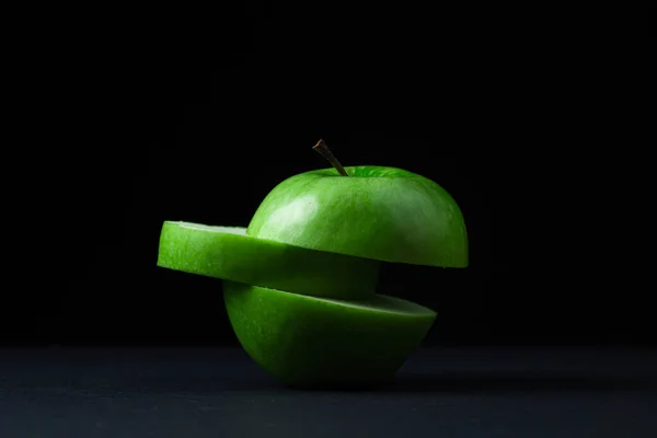 Green apple on a dark background. A cut green apple on a black background. Healthy food