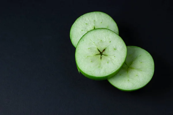 Green apple on a dark background. A cut green apple on a black background. Healthy food