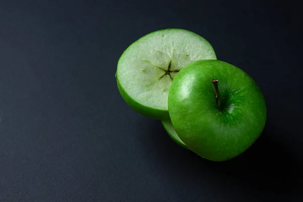 Green apple on a dark background. A cut green apple on a black background. Healthy food