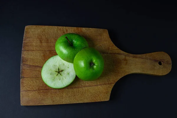 Green apple on a dark background. A cut green apple on a cutting board on a black background. Healthy food