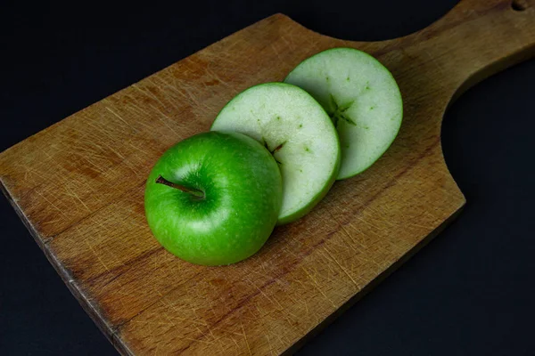 Green apple on a dark background. A cut green apple on a cutting board on a black background. Healthy food