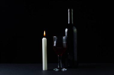Karanlık bir arka planda şarap ve mum. Siyah arka planda kırmızı şarabın yaratıcı bir fotoğrafı. Mum ışığında şarap.