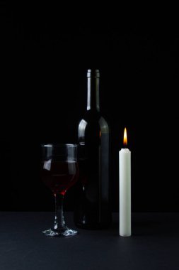 Karanlık bir arka planda şarap ve mum. Siyah arka planda kırmızı şarabın yaratıcı bir fotoğrafı. Mum ışığında şarap.