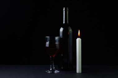 Karanlık bir arka planda şarap ve mum. Siyah arka planda kırmızı şarabın yaratıcı bir fotoğrafı. Mum ışığında şarap.