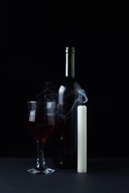 Karanlık bir arka planda şarap ve mum. Siyah arka planda kırmızı şarabın yaratıcı bir fotoğrafı. Şarap ve mum dumanı