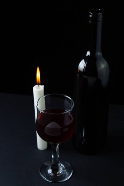 Karanlık bir arka planda şarap ve mum. Siyah arka planda kırmızı şarabın yaratıcı bir fotoğrafı. Mum ışığında şarap.