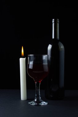 Karanlık bir arka planda şarap ve mum. Siyah arka planda kırmızı şarabın yaratıcı bir fotoğrafı. Mum ışığında şarap.