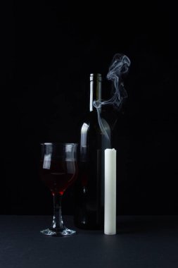 Karanlık bir arka planda şarap ve mum. Siyah arka planda kırmızı şarabın yaratıcı bir fotoğrafı. Şarap ve mum dumanı