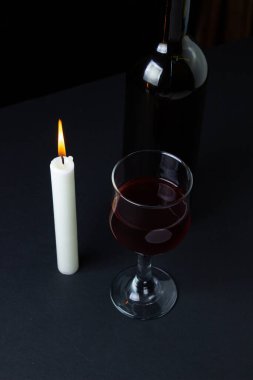 Karanlık bir arka planda şarap ve mum. Siyah arka planda kırmızı şarabın yaratıcı bir fotoğrafı. Mum ışığında şarap.