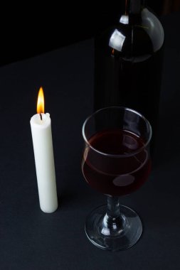 Karanlık bir arka planda şarap ve mum. Siyah arka planda kırmızı şarabın yaratıcı bir fotoğrafı. Mum ışığında şarap.