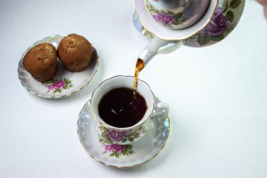 Çay bir fincana doldurulur. Beyaz masa örtüsü üzerinde bir fincan çay. Hafif kahvaltı. Çiçekli beyaz çay seti.