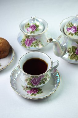 Beyaz masa örtüsü üzerinde bir fincan çay. Kekli çay. Hafif kahvaltı. Çiçekli beyaz çay seti.