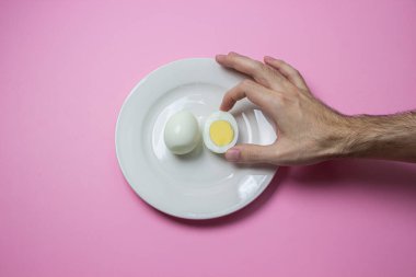 Haşlanmış yumurta tabakta ikiye bölünmüş. El yiyecek için uzanır. Sağlıklı kahvaltı. Pembe arka planda haşlanmış yumurta..