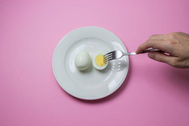 Haşlanmış yumurta tabakta ikiye bölünmüş. El yiyecek için uzanır. Sağlıklı kahvaltı. Pembe arka planda haşlanmış yumurta..