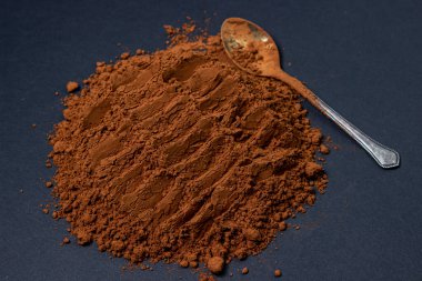 Siyah arka planda kakao tozu. Kaşık kakao tozunun içinde koyu bir arka planda yatıyor..