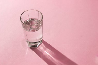 Pembe arka planda bir bardak su. Temiz içme suyu. Çevre dostu su