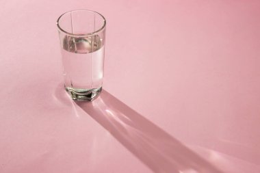 Pembe arka planda bir bardak su. Temiz içme suyu. Çevre dostu su