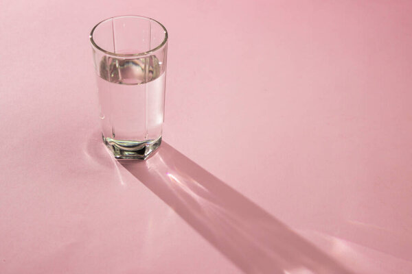 Стакан воды на розовом фоне. Чистая питьевая вода. Экологически чистая вода