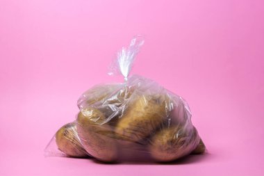 Pembe arka planda patatesli selofan çanta. Açık arkaplanda patates olan şeffaf bir paket. Ürünler çantada.