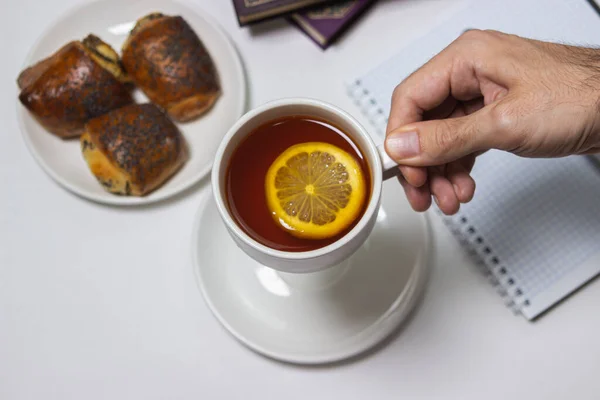 A cup of tea with lemon on a light background. Hand holds a cup of tea. Snack at work. A cup of tea at work.