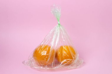 Pembe arka planda plastik poşetteki portakallar. Hafif arka planda portakallar. Portakal satın almak