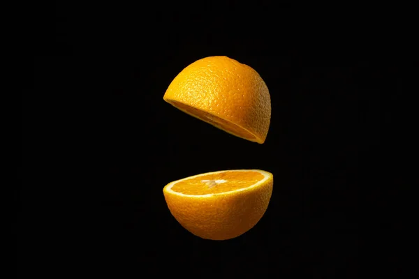 オレンジは暗い背景を背景に空中で半分にカットされます 黒の背景にスライスされたオレンジ オレンジの創造的な写真 — ストック写真