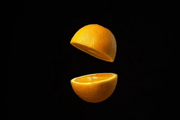 オレンジは暗い背景を背景に空中で半分にカットされます 黒の背景にスライスされたオレンジ オレンジの創造的な写真 — ストック写真