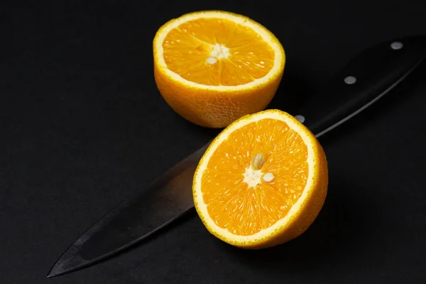 Sliced orange and knife on a black background. Creative photography of orange