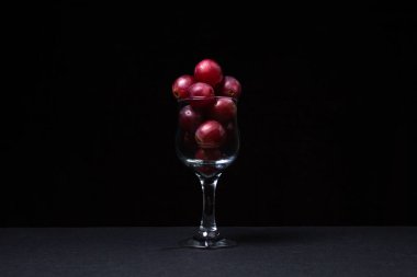 Pink grapes in a wine glass on a dark background. Large pink grapes on black background