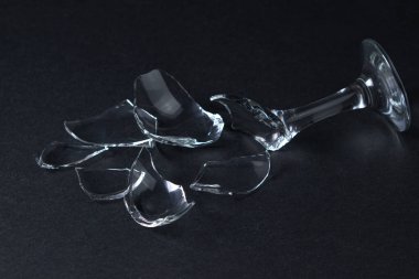 Broken wine glass on a dark background. Shards of a wine glass on a black background. Broken dishes