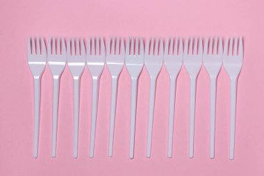 Pembe arka planda plastik çatallar. Tek kullanımlık sofra takımı. Plastik ürünler.
