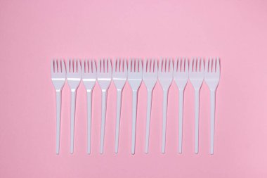 Pembe arka planda plastik çatallar. Tek kullanımlık sofra takımı. Plastik ürünler.